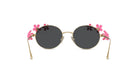 A pair of round sunglasses with black lenses and gold frames, adorned with pink flower decorations on the sides.