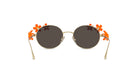 A pair of round sunglasses with dark lenses and gold frames adorned with orange flower decorations.