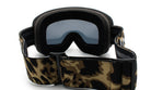 A pair of black and tan camouflage-patterned ski goggles with a black strap.